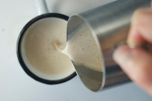 A hand is pouring freshly brewed chai into a white cup.
