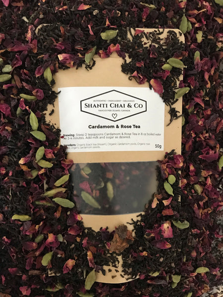Cardamom & Rose Tea is a beautiful and aromatic black tea blend containing Assam tea, cardamom pods and seeds and red rose petals. A package of Shanti Chai & Co's Cardamom & Rose Tea sits atop a pile of the green and pink blend!